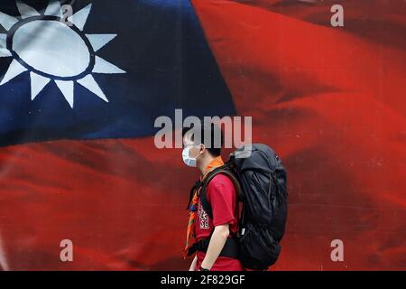 Taipei, Taipei, Taiwan. April 2021. Taiwanesen, die eine Gesichtsmaske tragen, gehen an einem riesigen Banner mit einer taiwanesischen Nationalflagge vorbei, inmitten zunehmender Spannungen mit China. Während Peking mehr Jet-Kämpfer auf die Insel schickt, sagte der taiwanesische Außenminister Joseph Wu, Taiwan werde sich bis zum „letzten Tag“ verteidigen, während es die Beziehungen zu den Vereinigten Staaten in den Bereichen Militär, Wirtschaft, Technologie und medizinische Dienste gefördert habe. Quelle: Daniel Ceng Shou-Yi/ZUMA Wire/Alamy Live News Stockfoto