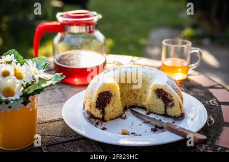 Marmorkuchen und Tee auf dem Tisch im Garten. Im Freien werden süße Speisen und heiße Getränke serviert Stockfoto