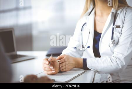 Unbekannte Ärztin verschreibt ihrem Patienten Antibiotika, während sie am Schreibtisch im Schrank in einer Klinik sitzen. Ärztin Stockfoto