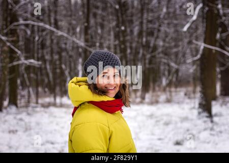 Schöne junge Frau trägt Wintermantel und Strickmütze im Schneewald. Lächelnde Frau, die im Winter geht Stockfoto