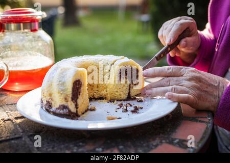 Ältere Frau serviert ein Stück Kuchen im Freien. Marmorgebundener Kuchen auf dem Picknicktisch Stockfoto