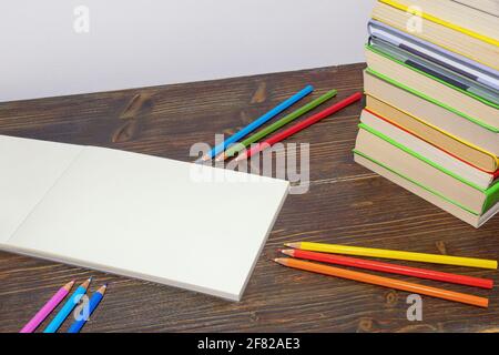 Bunte Buntstifte, Bücher und offenes Skizzenbuch auf dunklem rustikalem Tisch. Freier Speicherplatz für Text oder Bild Stockfoto