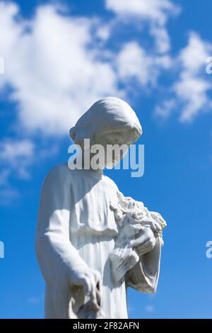 Weiße Gipskulptur, die eine Frau mit Blumen zeigt, Foto auf einem Friedhof Stockfoto