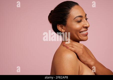 Seitenansicht einer attraktiven Frau, die vor rosa Hintergrund lächelt. Mischrasse Weibchen mit sauberer und klarer Haut. Stockfoto