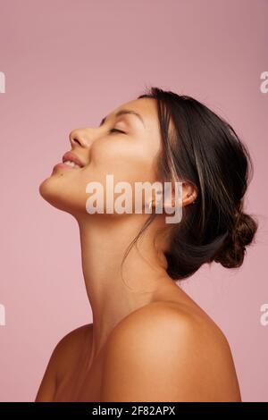 Nahaufnahme einer glücklichen jungen Frau mit gesunder Haut. Weibliche Modell mit geschlossenen Augen lächelnd über rosa Hintergrund. Stockfoto