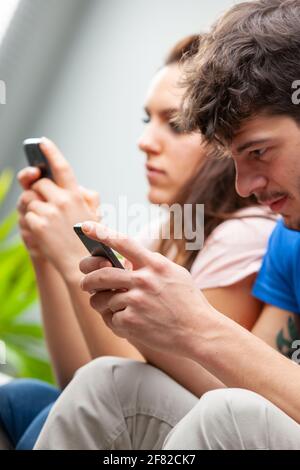 Junge Männer und Frauen, die ihre Mobiltelefone benutzen Während sie nebeneinander in einer Nahaufnahme sitzen Zugeschnittene Ansicht mit Fokus auf den Mann Stockfoto