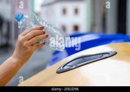 Nahaufnahme der weiblichen Hand, die Plastikflasche in den Recyclingbehälter wirft. Ökologisches Konzept mit Kunststoffabfällen. Umweltprobleme Stockfoto