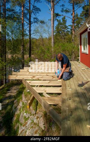 Ein Mann mit Schraubendreher, der Planken auf einem Holzdeck befestigt Stockfoto