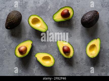 Eine kreative Draufsicht auf geschnittene und ganze Avocados Ein grauer Hintergrund Stockfoto