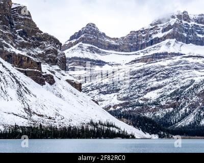 Hohe Berge mit Schnee hinter einem See im Winter mit Wolken Stockfoto