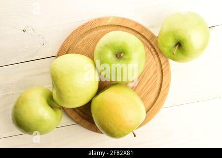 Eine Gruppe von mehreren saftigen Bio-, reifen, süßen, hellgrünen Äpfeln, auf einem runden Bambusblech, aus der Nähe, auf dem Hintergrund eines Holztisches Stockfoto