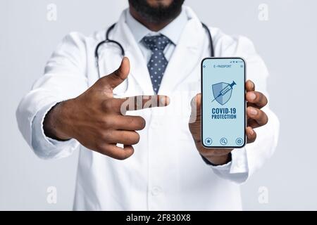 Schwarzer Arzt zeigt Smartphone mit immunem digitalen Pass für covid-19 Stockfoto