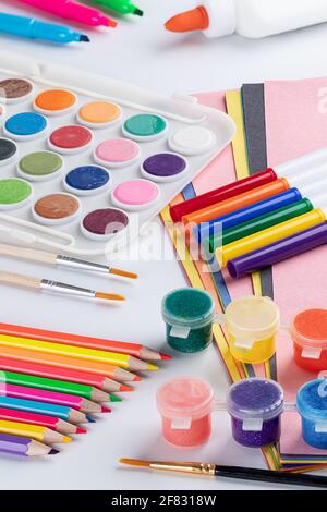 Bunte Schulkunst mit Buntstiften, Markern, Farbe und Papier auf einem weißen Tisch Stockfoto