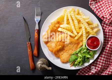 Teller mit gebratenem paniertem Hähnchenfleisch oder Schnitzel mit französisch Pommes und Salat auf dunklem Hintergrund Stockfoto