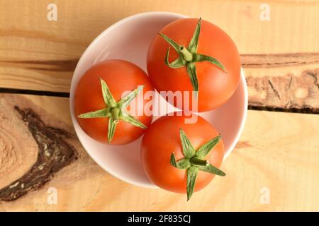 Drei saftige Bio-rote Tomaten in einer Keramikuntertasse, Nahaufnahme, auf einem Holztisch. Stockfoto