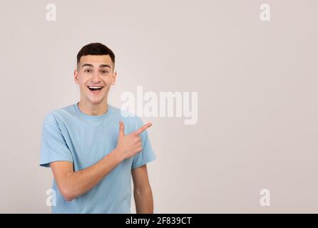 Glücklicher junger Mann in legerer Kleidung, der auf blank zeigt Raum auf grauem Studiohintergrund Stockfoto