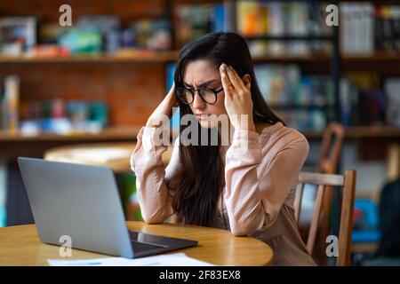 Termindruck. Erschöpfte lateinerin müde nach der Arbeit am Laptop, Kopfschmerzen habend, am Tisch im Café sitzend Stockfoto