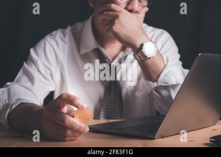 Geschäftsmann halten Bitcoin und beobachtet den Laptop mit Stress aufgrund von Verlusten aus dem Handel mit Bitcoin. Stockfoto