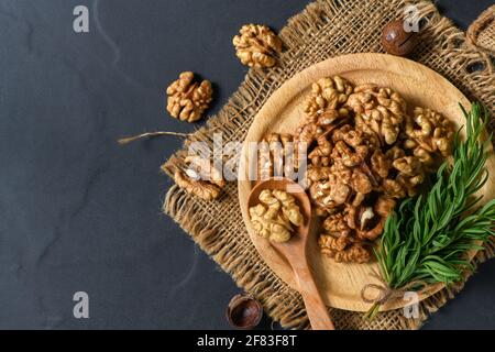 Walnüsse und Rosmarinblatt in Holzplatte auf schwarzem Tischhintergrund. Gesundes Nusskonzept. Walnüsse sind eine ausgezeichnete Quelle von Antioxidantien und includin Stockfoto