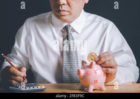 Geschäftsleute fallen ein Sparschwein mit Golden Bitcoin.electronic virtuelles Geld für Web-Banking und internationale Netzwerk-Zahlung, Stockfoto