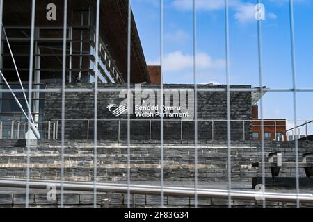 Cardiff Bay, Wales - 2021. April: Schild an der Wand des walisischen Parlamentsgebäudes, das hinter einem Drahtgefecht zu sehen ist. Stockfoto