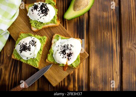 Sandwiches mit pochierten Eiern und Avocado auf dem Schneidebrett auf dem braunen Holzhintergrund. Draufsicht. Speicherplatz kopieren. Stockfoto