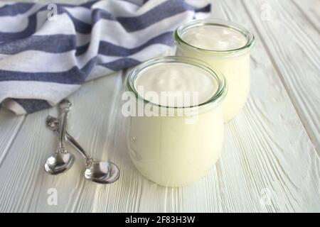 Natürlicher Milchjoghurt in den Gläsern auf dem weißen Holzhintergrund. Nahaufnahme. Stockfoto