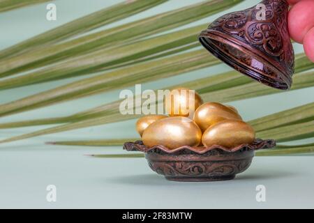 Religiöses islamisches Fest und heiliger Monat des Ramadan, EID KAREEM, Konzept: Eine braune metallische und verzierte Schale mit goldenen Mandel-Süßigkeiten. Palmblätter Stockfoto
