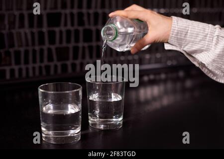 Mädchen gießt Wasser in ein Glas. Zwei Gläser mit Wasser gießen sauberes Wasser auf schwarzen Tisch Stockfoto