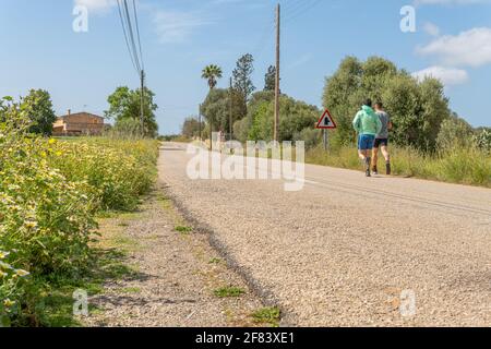 Campos, Spanien; april 10 2021: Landstraße im Landesinneren der Insel Mallorca mit zwei Teenagern auf dem Rücken, die beim Laufen üben Stockfoto