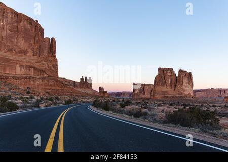 Asphaltstraße mit zwei gelben Linien in der Mitte von Eine rote Felsenschlucht im Sommer bei Sonnenaufgang Stockfoto