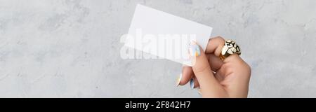 Gepflegte Womans Hand halten Postkarte auf grauem Beton Hintergrund Stockfoto