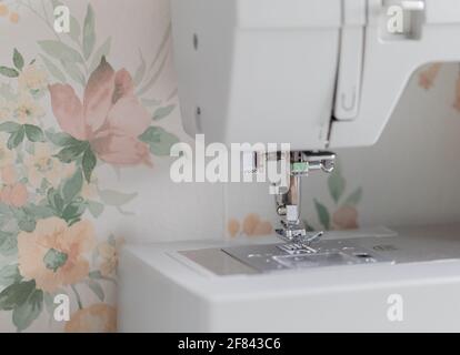 Nahaufnahme einer Nähmaschine mit Blumentapete dahinter Stockfoto