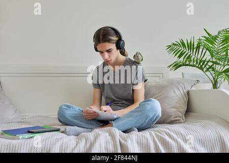 Männlicher Teenager mit grünem Papagei auf der Schulter, mit Lehrbüchern Stockfoto