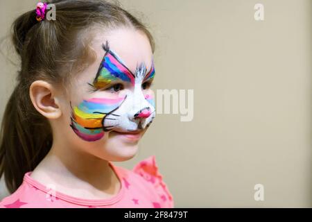 Kind mit Gesichtsbemalung von Kitty, nettes kleines Mädchen mit gemalter Maske auf dem Gesicht der Regenbogenkatze. Portrait von hübschen Kind mit schönen Make-up und Kopie sp Stockfoto