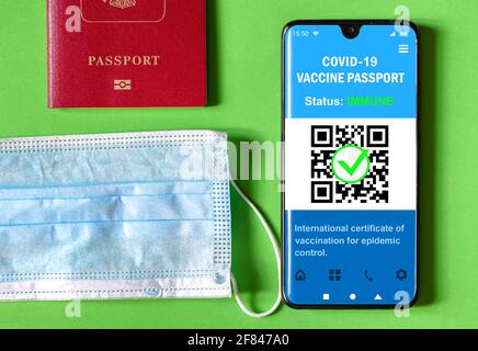 Gesundheitspass der COVID-19-Impfung in Handy, Maske und Touristenpass. Impfpass-App auf dem Smartphone für Reisen. Digital Coronavi Stockfoto