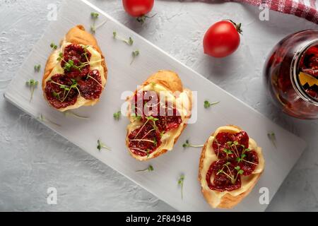 Sandwich mit sonnengetrockneten Tomaten, hausgemachter Mayonnaise und Mikrogemüse, serviert auf einem Brett auf grauem Hintergrund Stockfoto