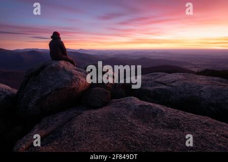 Ein Wanderer genießt einen wunderschönen und farbenfrohen Sonnenaufgang vom Old Rag Mountain im Shenandoah National Park. Stockfoto
