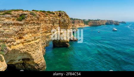 Blick auf Klippen aus zerklüfteten Sandsteinfelsen, Felsformationen im türkisfarbenen Meer, Sandstrand auf der Klippe, Praia da Marinha, Algarve, Lagos, Portugal Stockfoto