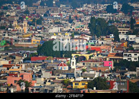 Landschaft mit landschaftlicher Aussicht auf die Innenstadt von Cholula mit der farbenfrohen Kolonialarchitektur, die von der Großen Pyramide in Puebla, Mexiko, aus gesehen wird. Stockfoto