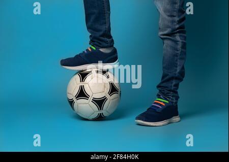 Nahaufnahme eines nicht erkennbaren Jungen, der auf einem Fußball steht, isoliert auf blauem Hintergrund mit Kopierfläche Stockfoto