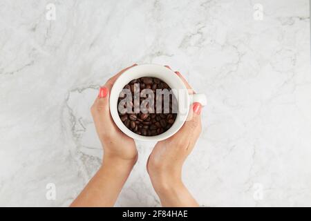 Hält eine Tasse Kaffeebohnen auf einem Marmorboden High-Angle-Ansicht Stockfoto