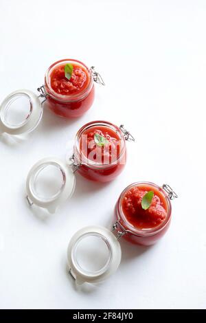 Hausgemachte Tomatensauce mit Basilikum in Gläsern isoliert auf weißem Hintergrund. Direkt darüber. Stockfoto