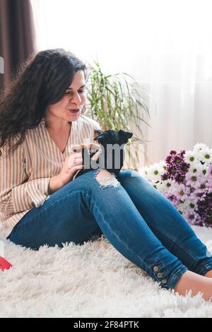 Die junge glückliche Frau spielte mit einem niedlichen kleinen Welpen. Schwarzer und brauner Miniatur-Pinscher in der weiblichen Hand Stockfoto