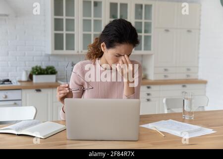 Müde junge lateinische weibliche abgelenkt von Laptop reiben Nase Brücke Stockfoto