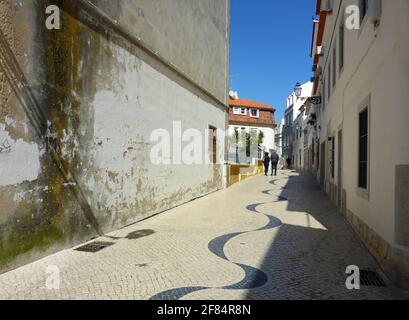 Eine interessante schmutzige Wand in einer alten Straße mit Kopfsteinpflaster in einem Wellenmuster. Cascais ist ein beliebtes Touristenziel Stockfoto