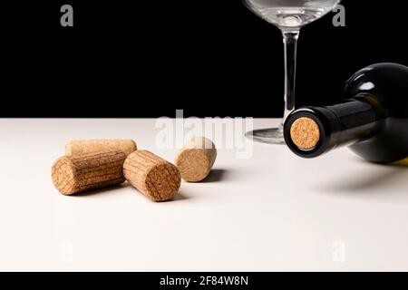 Flasche Weißwein und Korken auf weißem Tisch vor schwarzem Hintergrund. Selektiver Fokus, minimalistische, lebendige Farben. Stockfoto