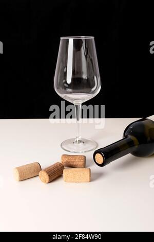 Flasche Weißwein und Korken auf weißem Tisch vor schwarzem Hintergrund. Selektiver Fokus, minimalistische, lebendige Farben. Stockfoto