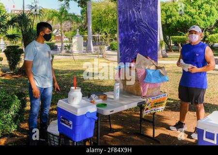 Mann, der während der Covid-19-Pandemie Tacos von einem Straßenhändler kauft. Straßenhändler in Merida Mexiko arbeiten mit verstärkten Hygienemaßnahmen, um die Ausbreitung des tödlichen Virus einzudämmen. Stockfoto