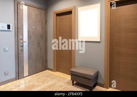 Moderner Eingangsbereich in neutralen Braun- und Grautönen. An der Wand befindet sich der Fotorahmen mit Mockup, die Eingangstür mit Gegensprechanlage. Concept Fashion Stockfoto